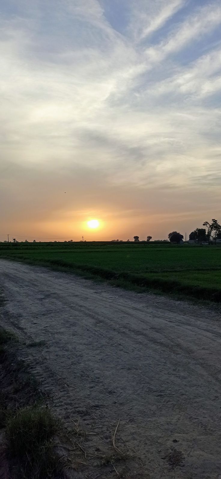 the sun is setting over an empty dirt road