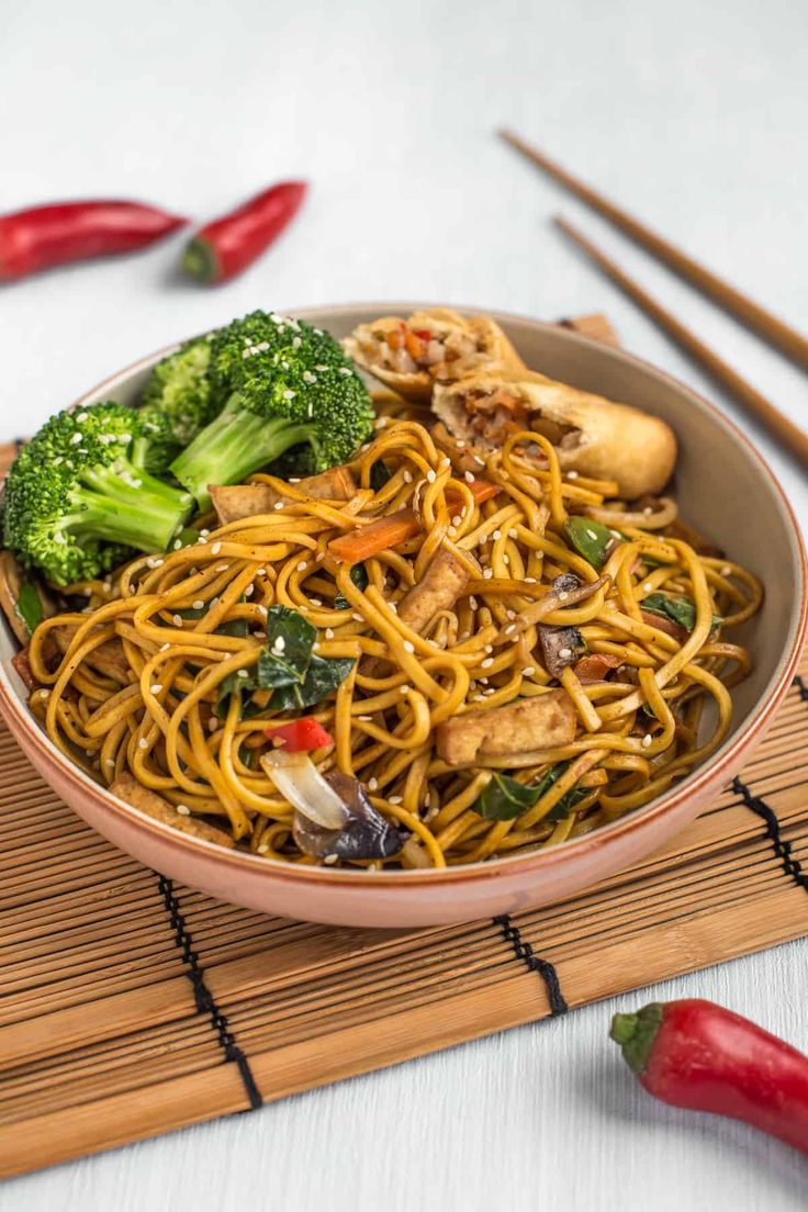 a bowl filled with noodles, broccoli and other vegetables on top of a bamboo mat