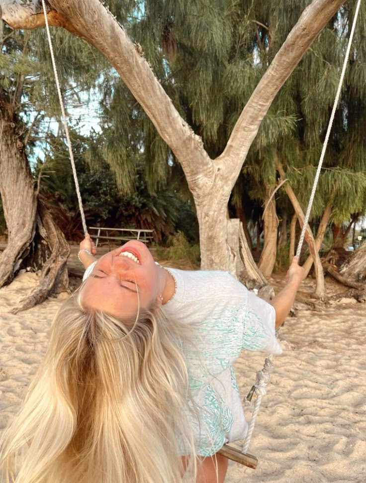 a woman laying on a swing in the sand near a tree with no leaves or branches