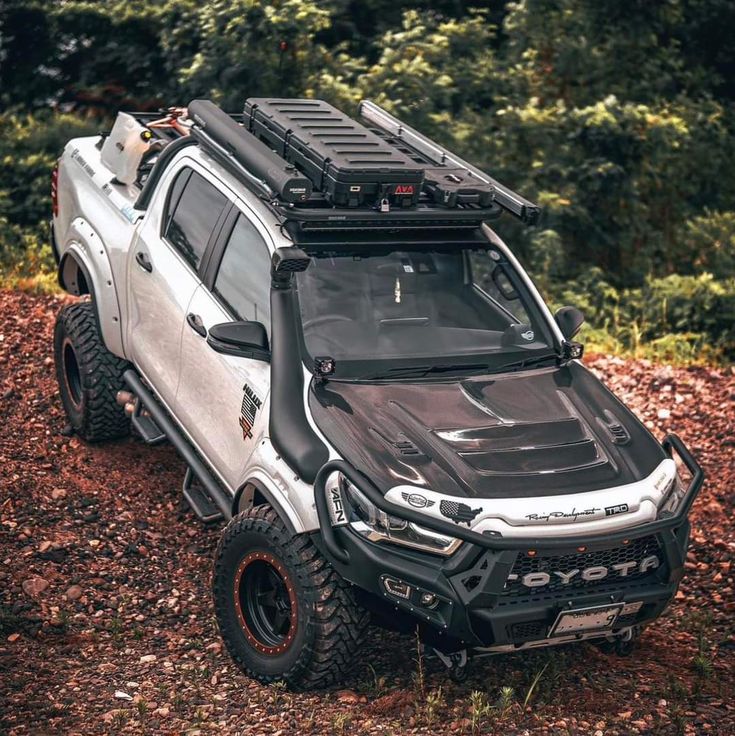 a white truck parked on top of a pile of dirt next to trees and bushes