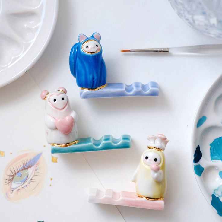 three little figurines sitting on top of a white table next to paintbrushes