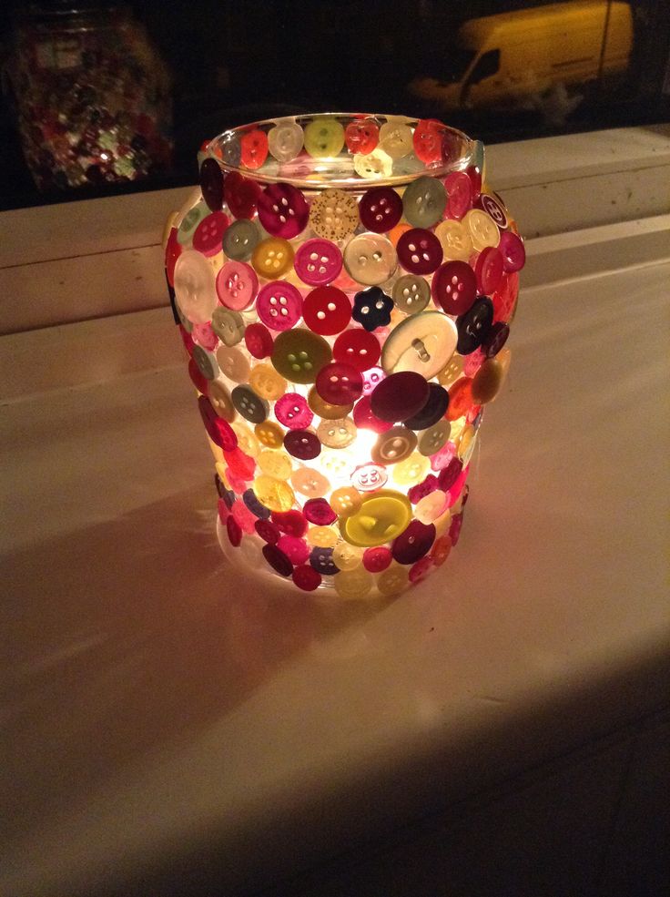 a glass vase with buttons on it sitting on a table next to a window sill