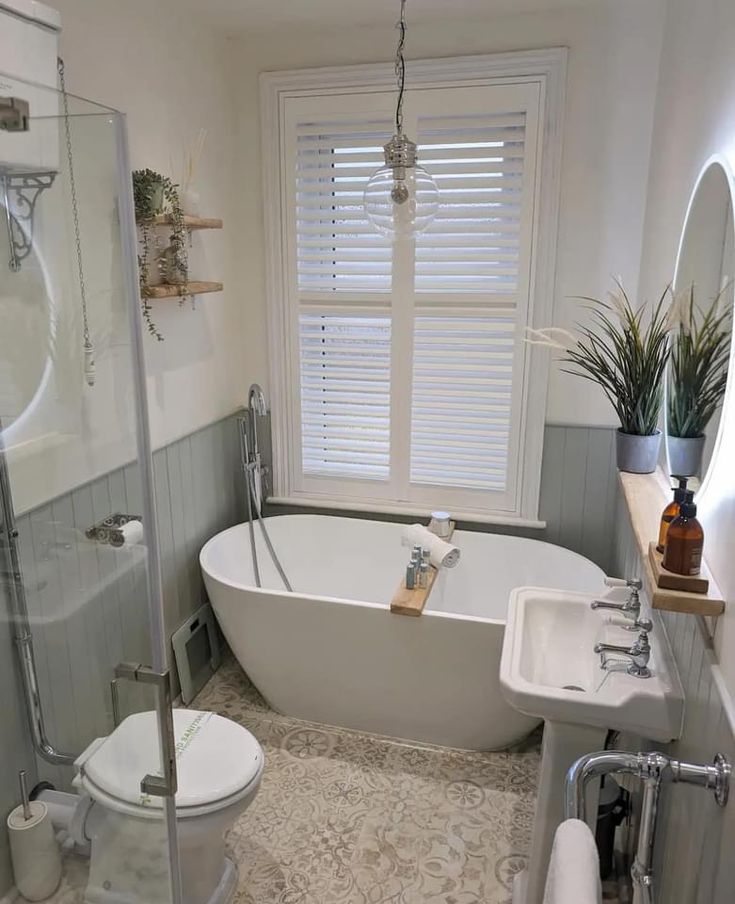 a white bathtub sitting next to a toilet and sink in a bathroom under a window