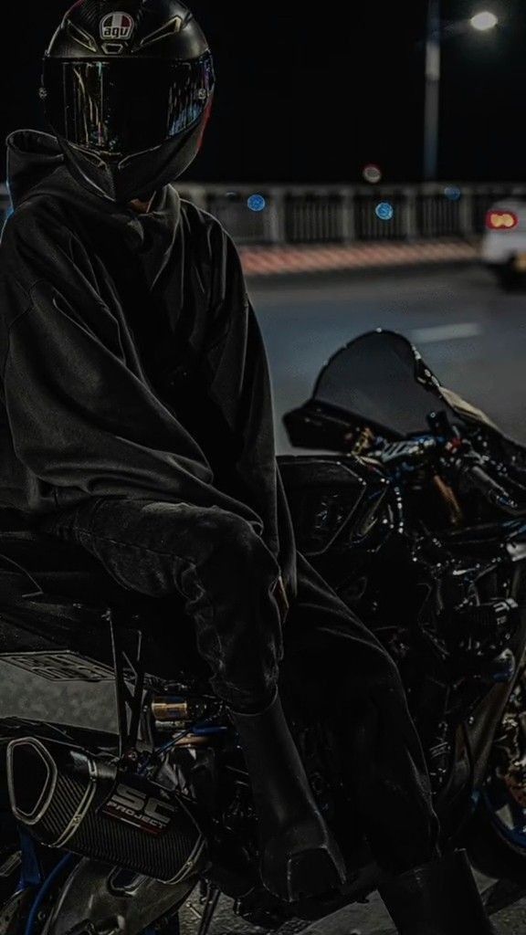 a person sitting on a motorcycle in the street at night wearing a black jacket and helmet