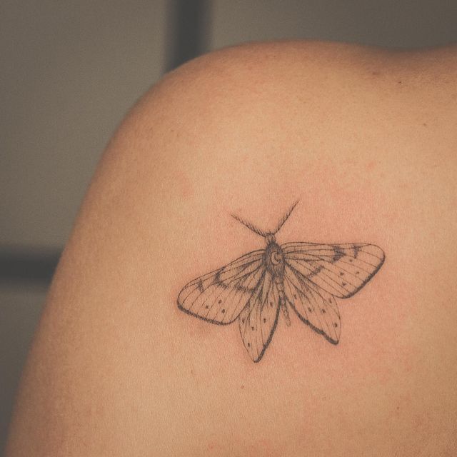 a small moth tattoo on the back of a woman's shoulder