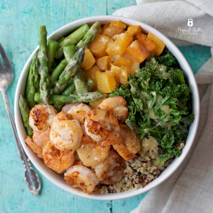 a white bowl filled with shrimp, broccoli and other vegetables next to a fork