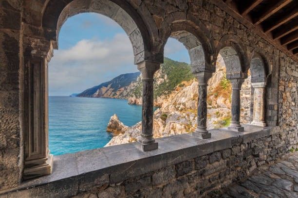 an old stone building overlooking the ocean with arches and pillars in front of it, looking out