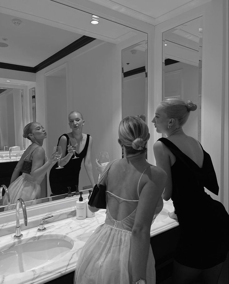 three women standing in front of a bathroom mirror looking at each other's reflection