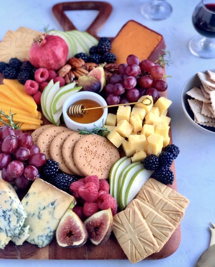 an assortment of cheeses, crackers and fruit on a cutting board