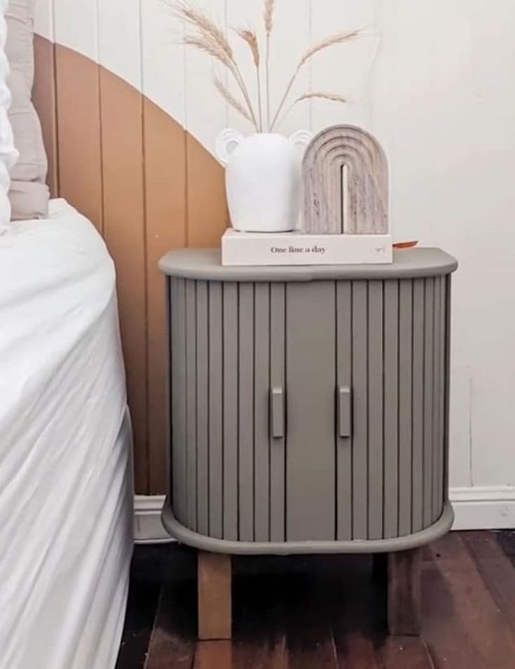 a small cabinet next to a bed in a room with wood flooring and white walls