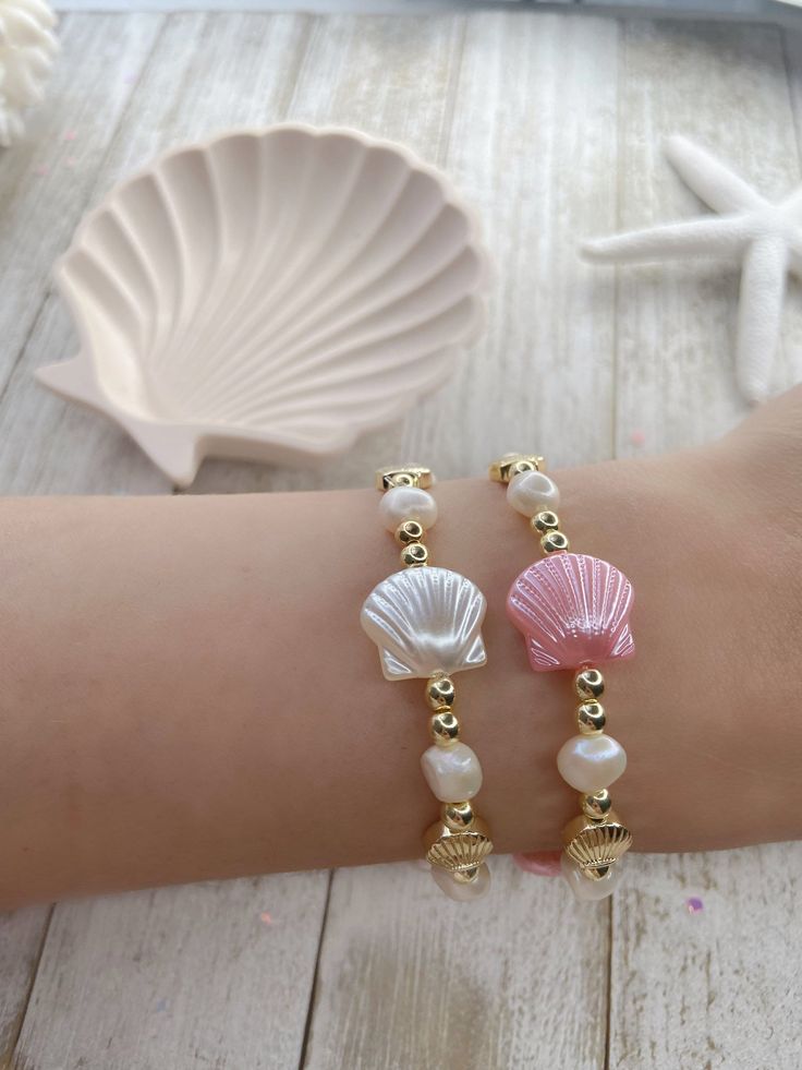 two bracelets with seashells and pearls are on the arm of a woman