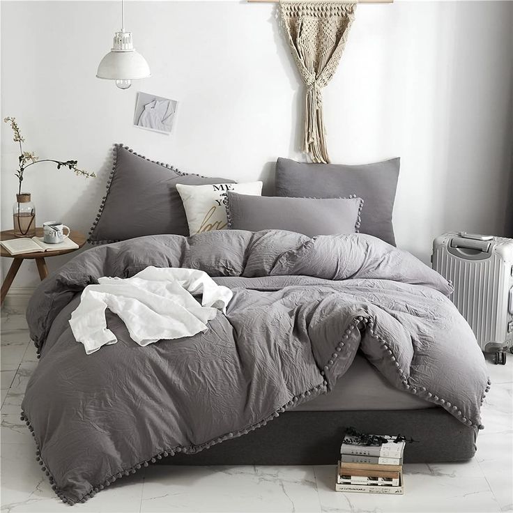 a bed with grey comforter and pillows in a white room next to a radiator