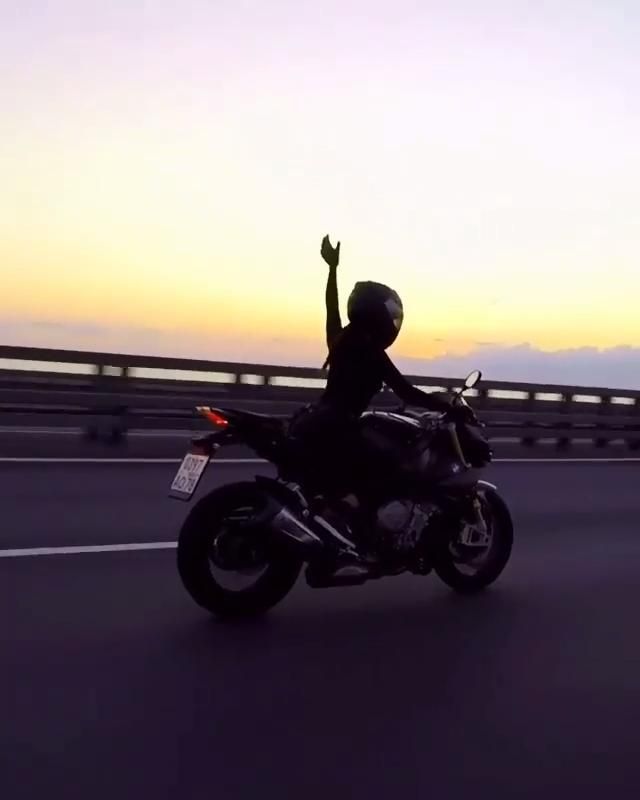 a person riding on the back of a motorcycle down a highway at sunset with their arms in the air