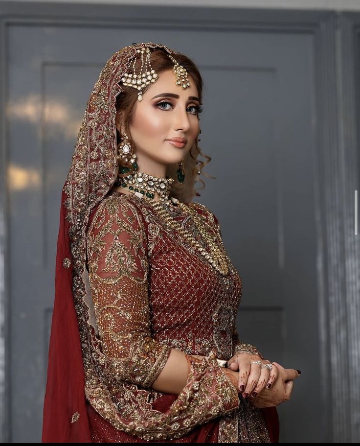 a woman in a red and gold bridal outfit posing for the camera with her hands on her hips