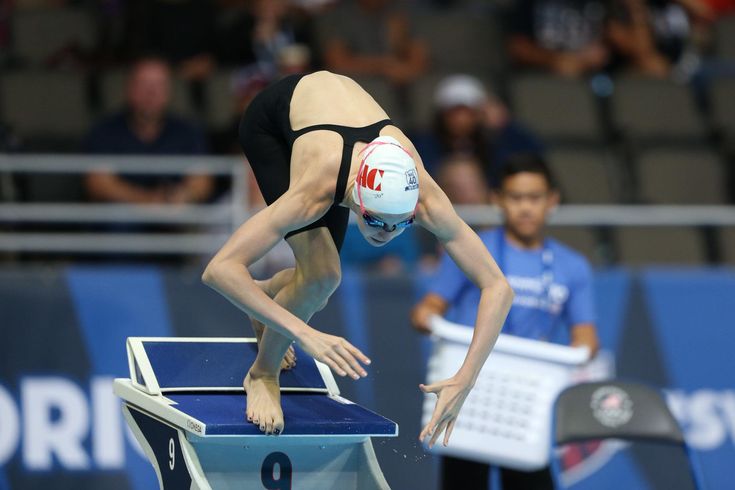 a woman diving into a pool with a ball in her hand and people watching from the stands