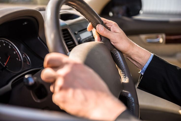 a man driving a car with his hand on the steering wheel and holding the steering wheel