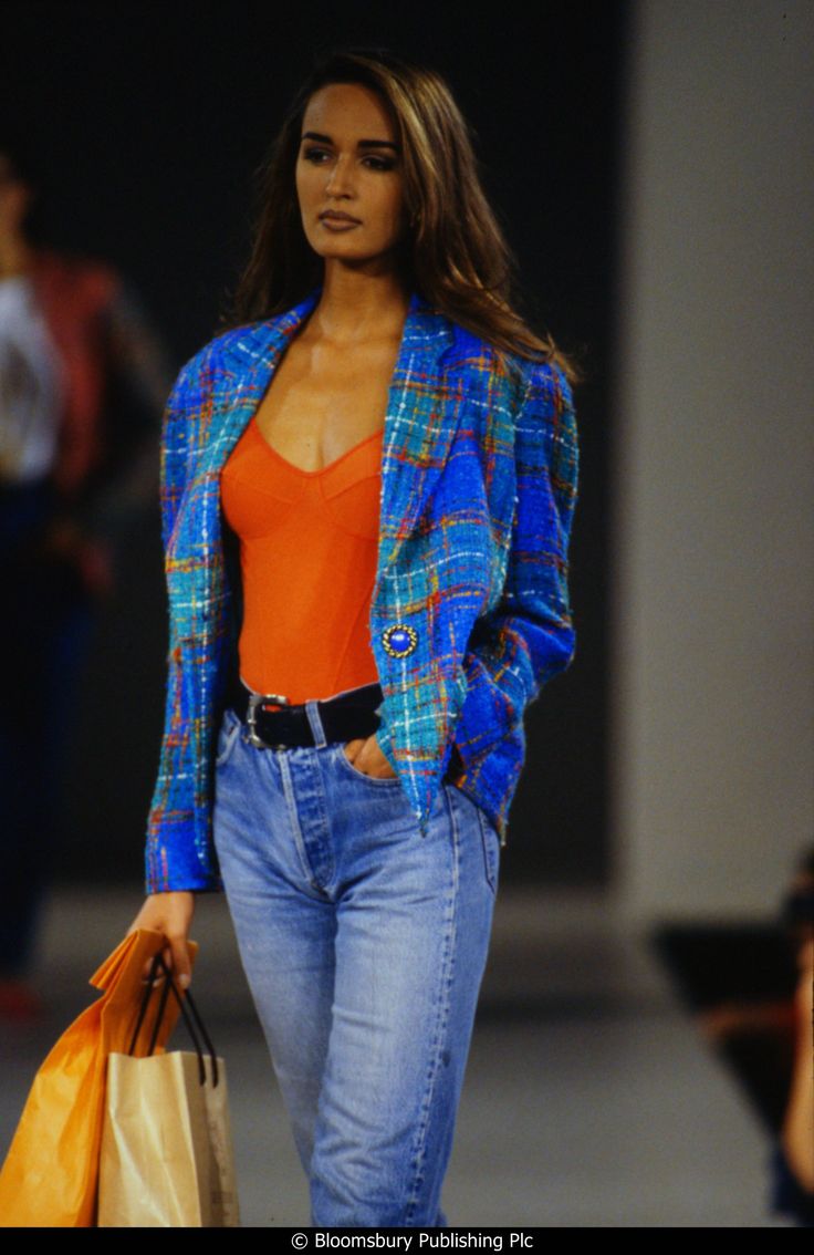 a woman is walking down the runway carrying shopping bags and looking at someone behind her