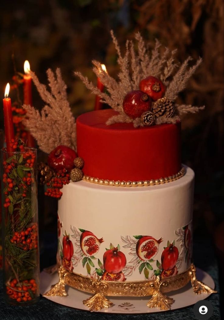 a three tiered cake with pomegranates on it and candles in the background