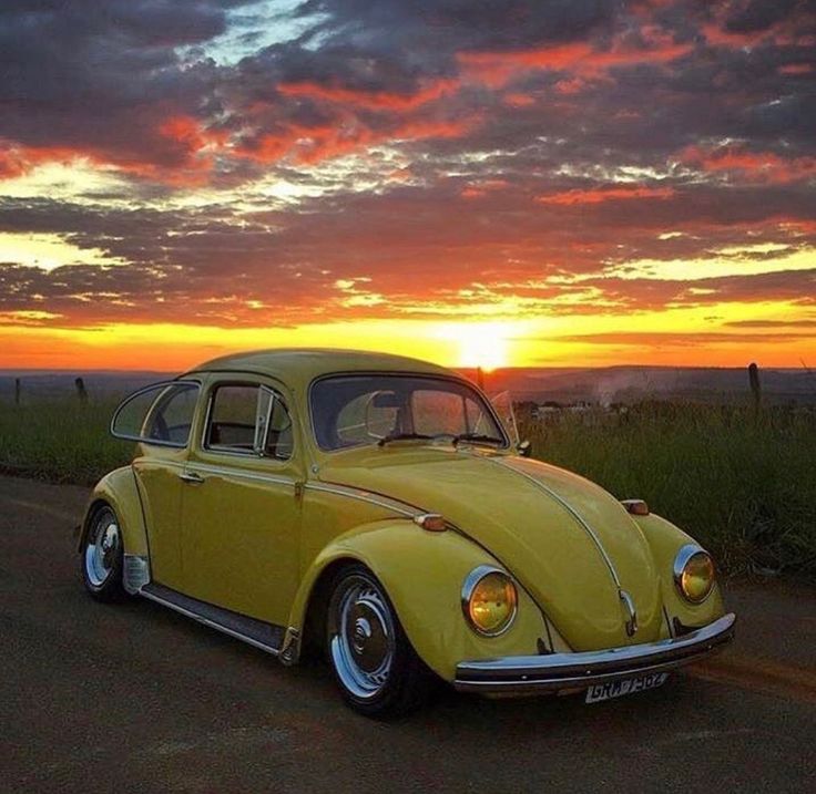 a yellow vw bug is parked on the side of the road at sunset or dawn