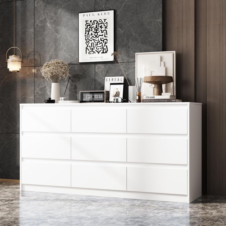 a white dresser sitting in a living room next to a wall with pictures on it