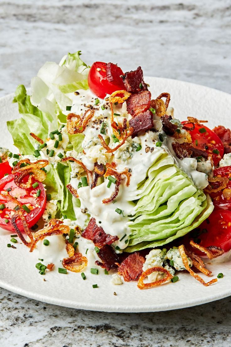 a salad with bacon, lettuce and tomatoes on a white plate sitting on a table