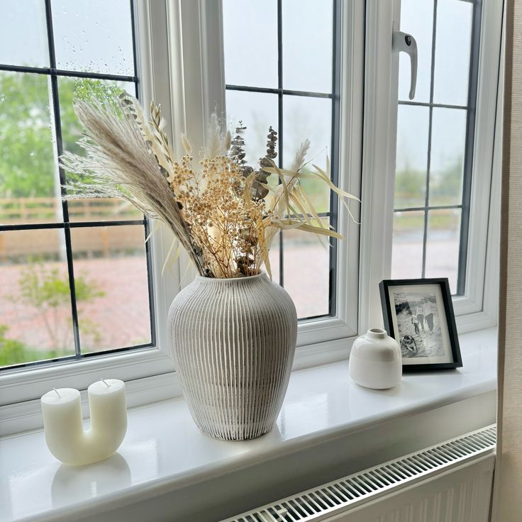 a vase with some flowers on a window sill next to two candles and a picture