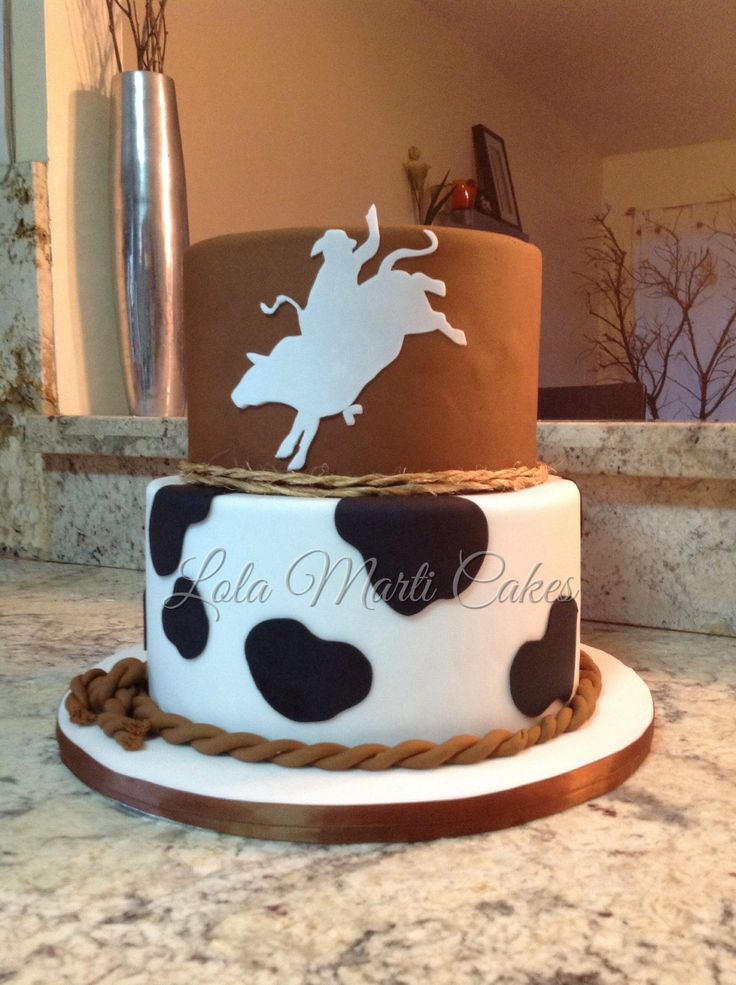 three tiered cake decorated with black and white cow print on the top, brown rope around the bottom