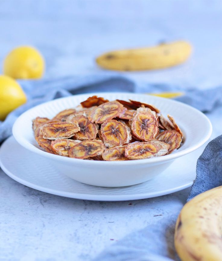 a white bowl filled with sliced bananas on top of a blue cloth next to some lemons