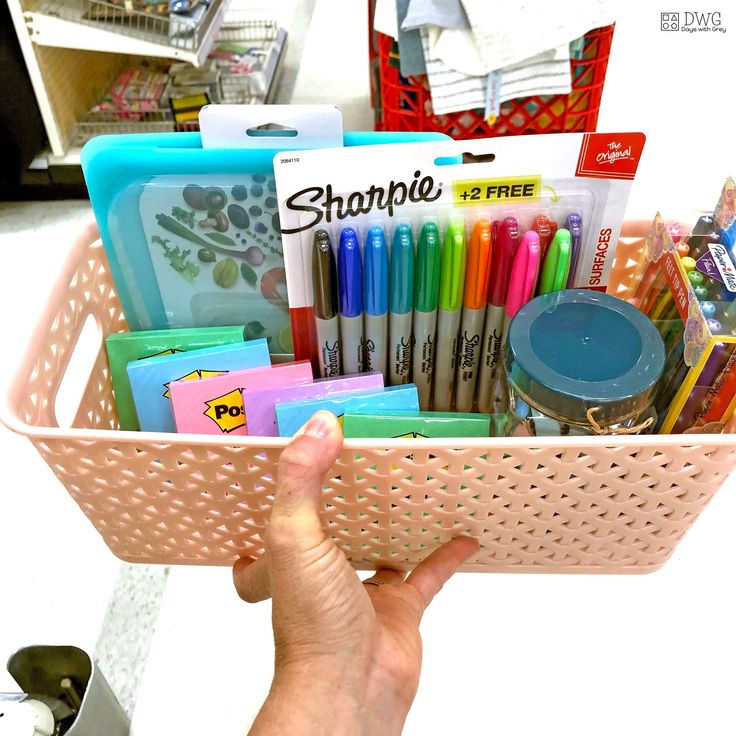 a person holding a pink basket filled with school supplies and writing utensils in it