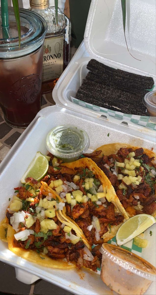 two tacos in a styrofoam container with lime wedges on the side