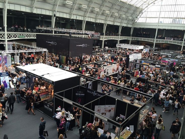 a crowd of people standing around a booth at a trade show in an indoor building