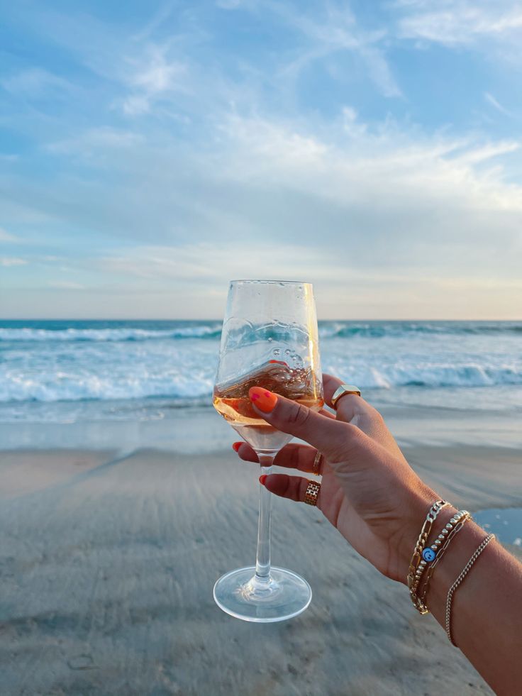 a person holding up a wine glass on the beach