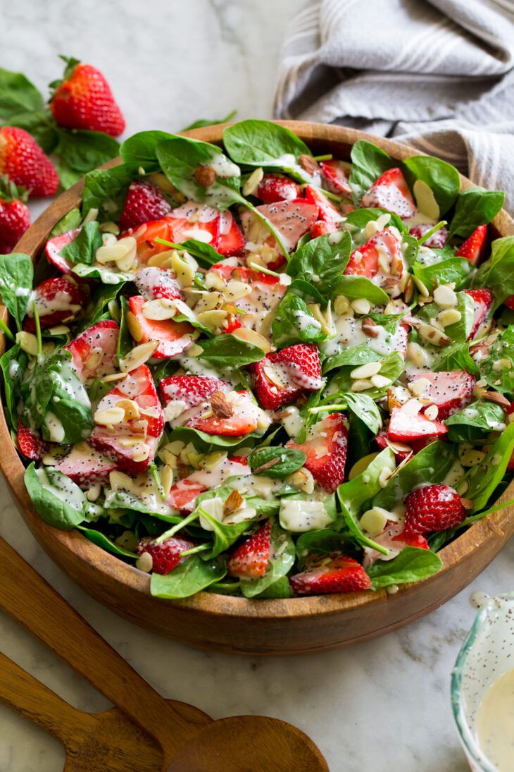 a salad with spinach, strawberries and almonds in a wooden bowl on a marble table