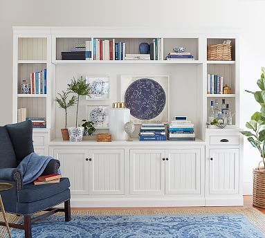 a living room filled with furniture and bookshelves next to a blue rug on top of a wooden floor