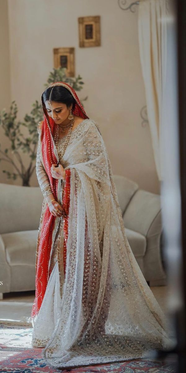 a woman in a red and white sari is looking down at her wedding dress