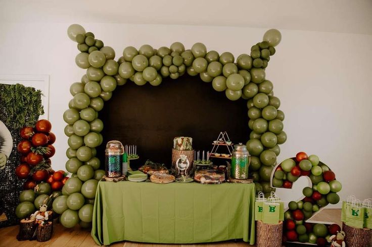 a green table topped with lots of food and balloons in the shape of an arch