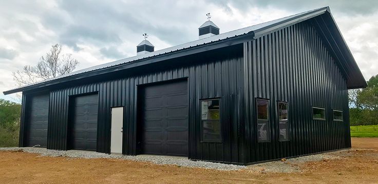 a large black building with two doors and windows on the side of it, in front of a grassy field