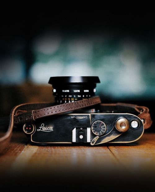 a camera sitting on top of a wooden table next to a leather strap and lens