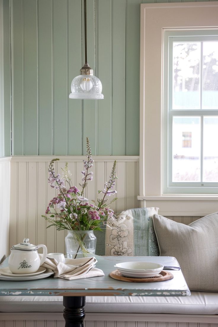 a table with plates and flowers on it in front of a window next to a bench