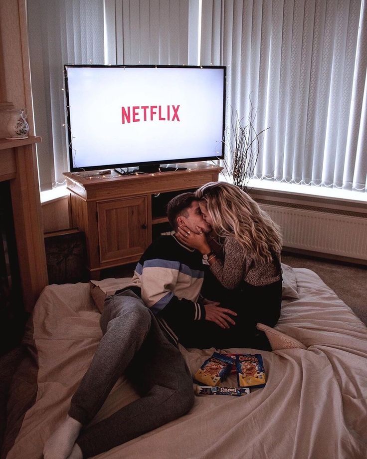 two people sitting on a bed in front of a television with the netflix logo on it