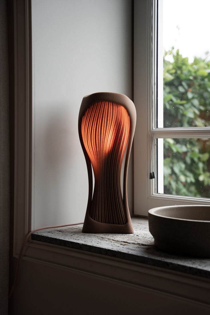 an orange lamp sitting on top of a window sill next to a bowl