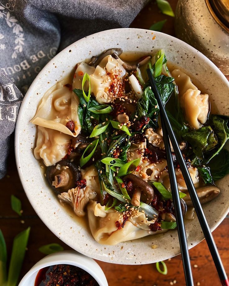 a bowl filled with noodles and vegetables next to chopsticks on a wooden table