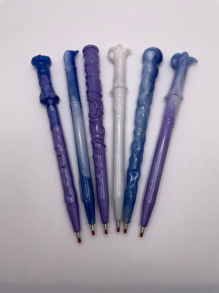 five different colored pens are lined up on a white surface, one is purple and the other is blue