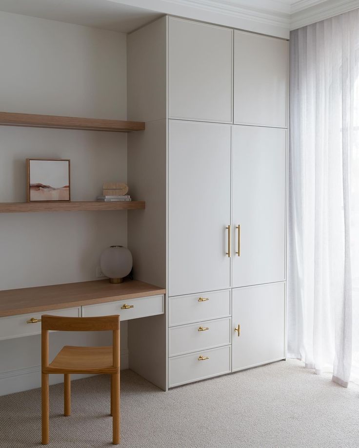 a bedroom with white walls and wooden shelves next to a desk in front of a window