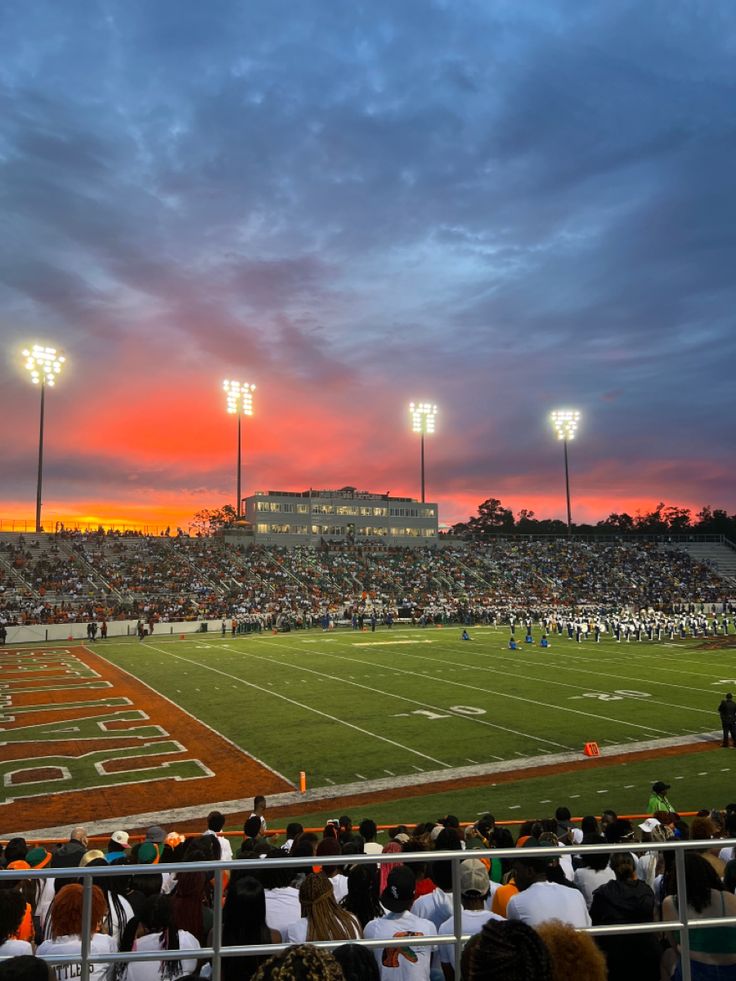 the sun sets over a football field as people sit in bleachers watching it