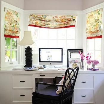 a desk with a computer on top of it next to two windows covered in curtains