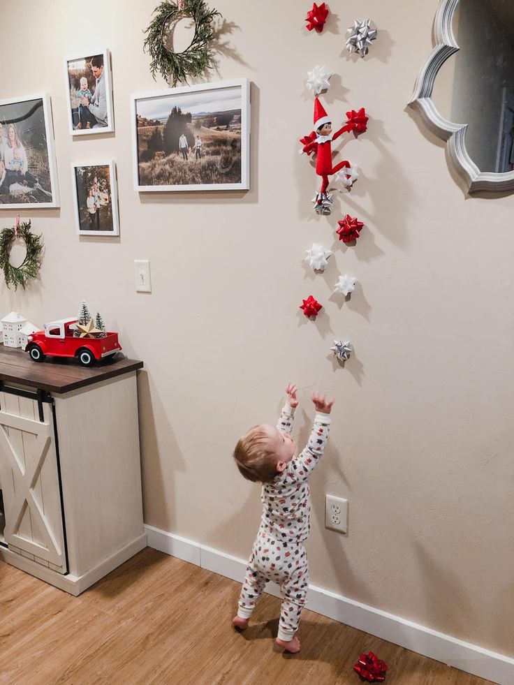 a toddler reaching up to reach the christmas decorations on the wall above him,