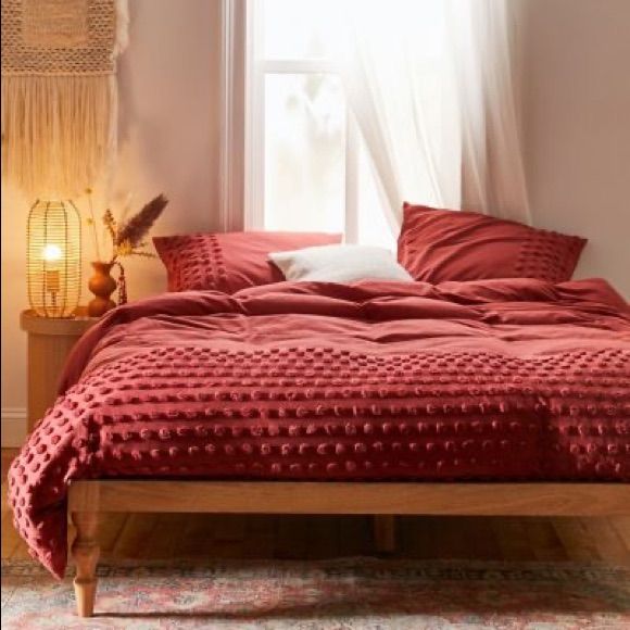 a bed with red sheets and pillows in a bedroom next to a lamp on a table