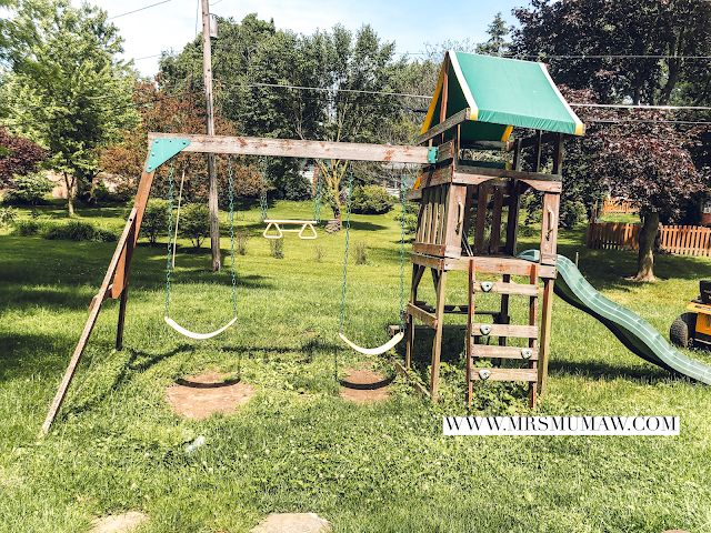 a wooden swing set in the middle of a grassy area with swings and climbing ropes