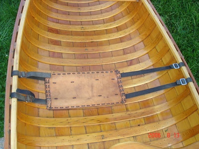 a wooden canoe with two oars and leather straps on the bottom row, sitting in grass